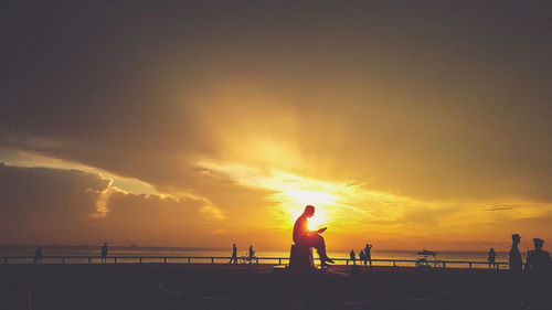 Silhouette people on beach against sky during sunset