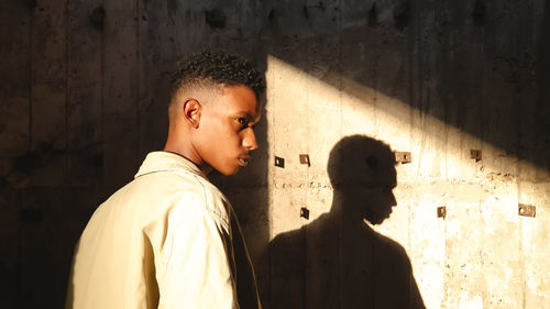 Side view of young man standing against wall