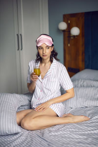 Woman in pajamas and with a sleep mask on the bed in the bedroom and drinking orange juice 