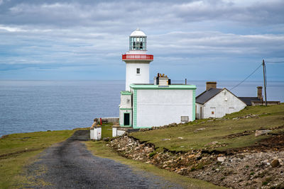 Lighthouse amidst sea and buildings against sky