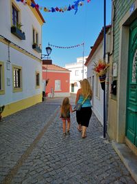 Rear view of women walking on street amidst buildings in city