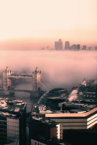 High angle view of city by river at sunset during foggy weather