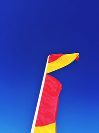 Low angle view of lifeguard flag against blue sky