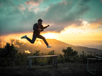 Full length of man jumping over field against sky during sunset