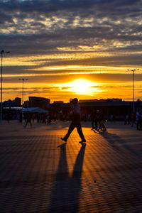 Silhouette man walking on city street during sunset