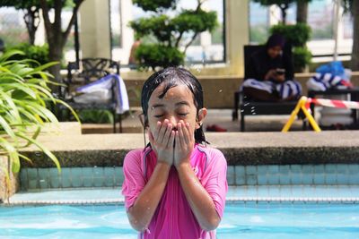 Wet girl covering mouth while standing in swimming pool