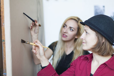 Portrait of smiling young woman holding camera against wall