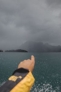 Person hand by sea against sky