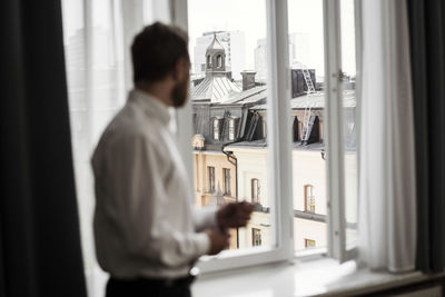 Side view of businessman looking at buildings through window from hotel room