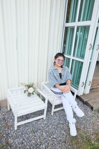 Portrait of young woman sitting on chair against house