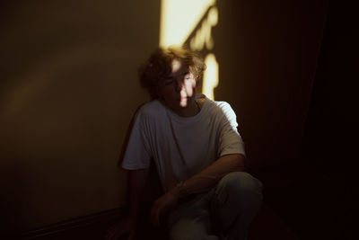 Young woman looking away while sitting against wall at home