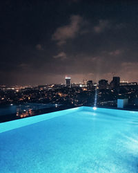 Illuminated city by sea against sky at night