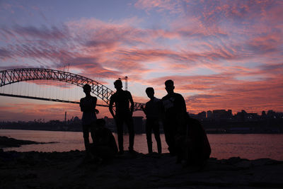 Silhouette friends standing by river in city during sunset