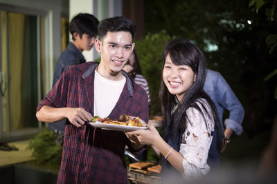 Smiling friends having meal at backyard during night