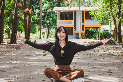 Portrait of smiling young woman throwing leaves while sitting on road in forest