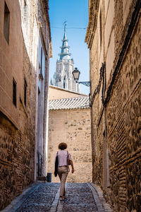 Rear view of woman walking in alley amidst buildings