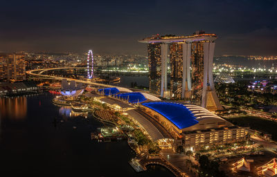 Aerial view of illuminated buildings by sea against sky at night