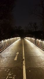 Road amidst bare trees at night