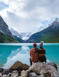 Rear view of woman sitting on rock by lake against mountain