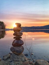 Stack of stones on beach against sky during sunset