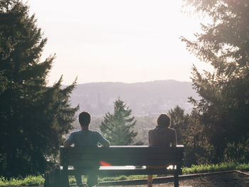 Rear view of man and woman sitting on bench at observation point against sky