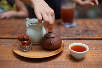 Close-up of cropped hand holding teapot tea by nuts in plate on table