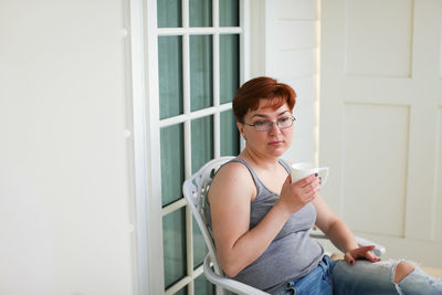 Young woman using mobile phone while sitting on window