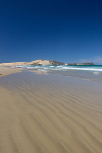 Scenic view of beach against clear blue sky