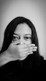 Portrait of young woman covering mouth with hand against wall