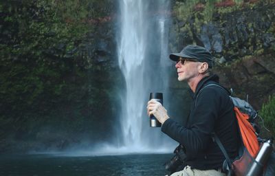 Side view of man looking away against waterfall