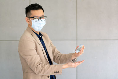 Portrait of man holding sanitizer and standing against wall