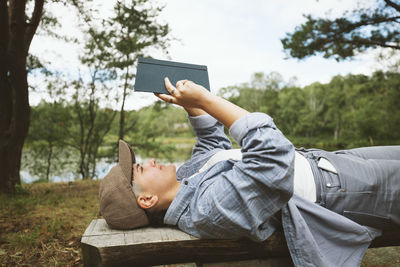 Young woman reading book while lying on wooden bench