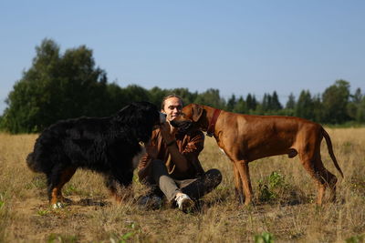 Portrait of man sitting with dogs on land against clear sky