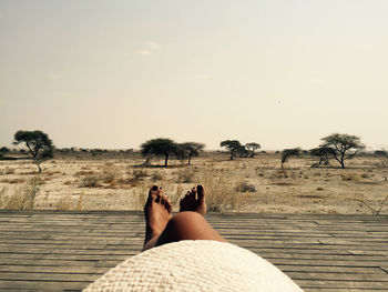 Low section of woman relaxing on field against sky