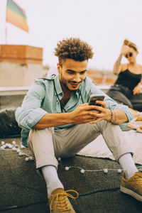 Smiling young man using smart phone while sitting on terrace at party