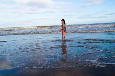 Rear view portrait of girl standing on beach against sky
