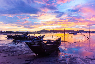 Boat moored on shore against sky during sunset