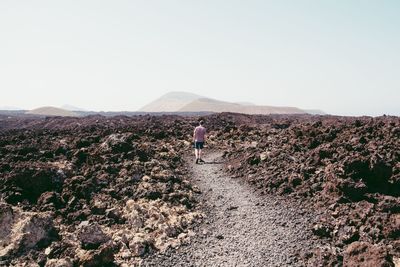 Rear view of man walking on rocky landscape against clear sky