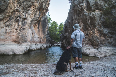 A tourist with a pet with his back to the camera on the river bank