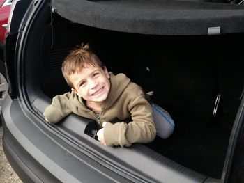 Portrait of happy boy sitting in car trunk