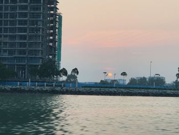 Sea by swimming pool against buildings at sunset