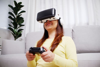 Young woman using phone while standing on sofa at home