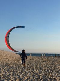 Rear view of man standing on beach against clear sky