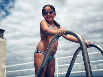 Smiling girl standing by railing against sky