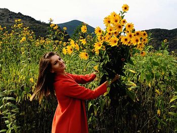 Side view of woman holding sunflowers while standing at farm