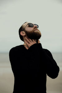 Young man wearing sunglasses standing against sea