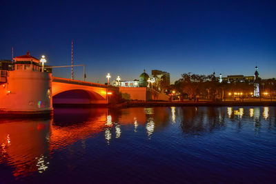 Illuminated buildings by river against sky at night