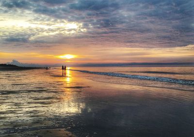 Silhouette people on beach against sky during sunset