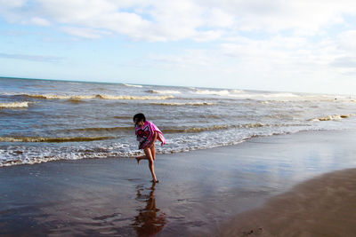 Full length of girl running on beach against sky