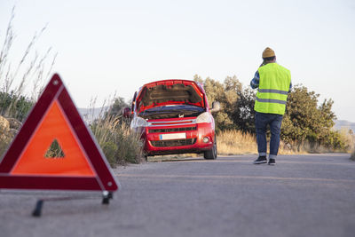 Man with relaxed attitude stranded on the road next to the broken down car talking on the phone